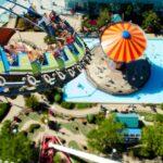Eine Achterbahn mit Fahrgästen, die über einen Freizeitpark mit einem bunten Pavillon und einem Pool fährt.