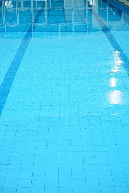 Blick auf die Wasseroberfläche eines Schwimmbades mit blauen Fliesen und Lichtreflexionen.