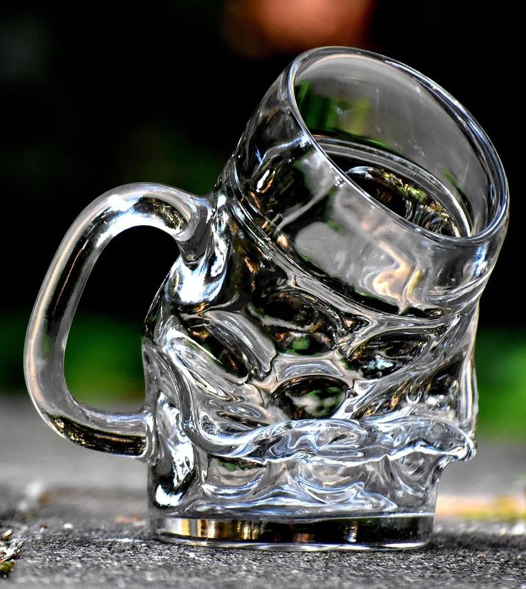 Ein klarer Glasbierkrug, leicht geschmolzen, nach vorne geneigt, auf dem Boden stehend.